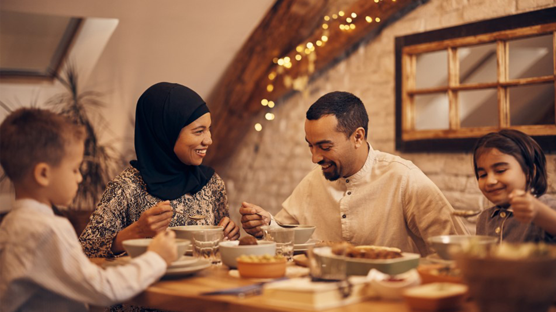 Family enjoying a warm home-cooked meal together at a cozy dining table with festive lights in the background.