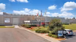 Front entrance of Unilever’s Raeford, USA facility with flagpoles, landscaped grounds and a parked vehicle under a bright blue sky.